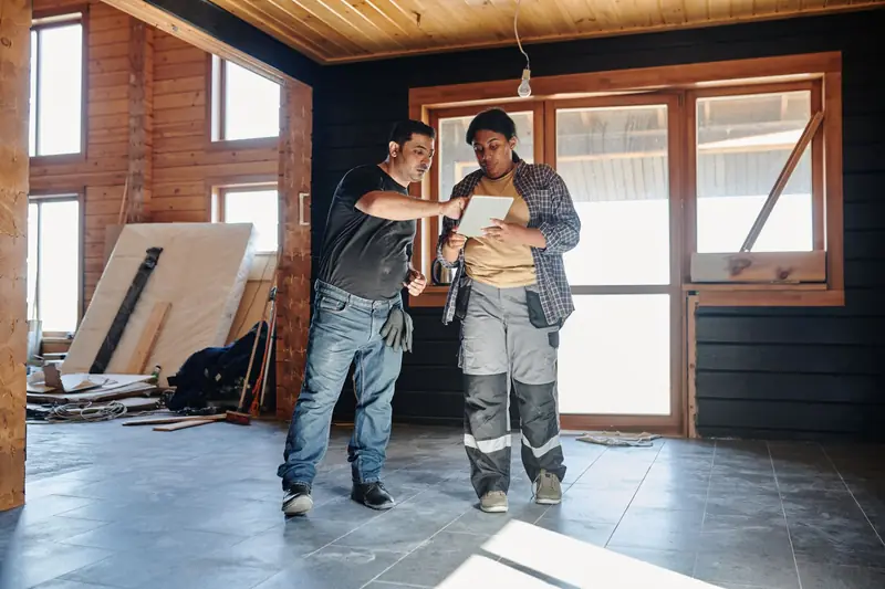 Twee vakmensen bekijken renovatieplannen op een tablet in een woning in verbouwing