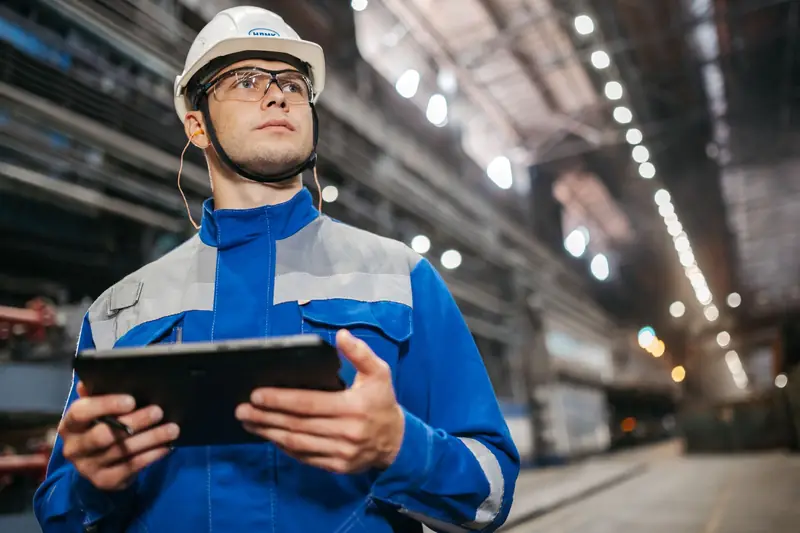 Technicus met veiligheidshelm gebruikt een tablet in een grote productiehal