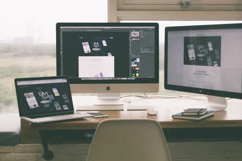Werkplek met twee beeldschermen en een laptop waarop een webdesignproject open staat